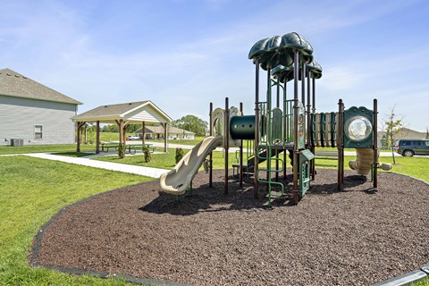 Three Bedroom Townhomes In Blue Springs, MO - Chapman Ridge Townhomes - A Playground Includes Multiple Slides, Soft Mulch Ground, Picnic Tables, Sidewalk Paths, And Green Lawn.