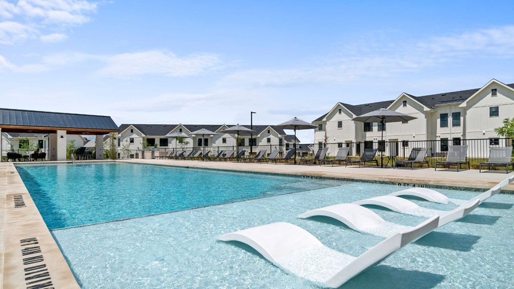 a swimming pool with chaise lounge chairs in front of apartment buildings