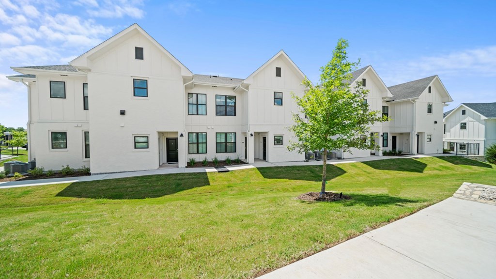 a group of white houses with grass and a tree in front of them