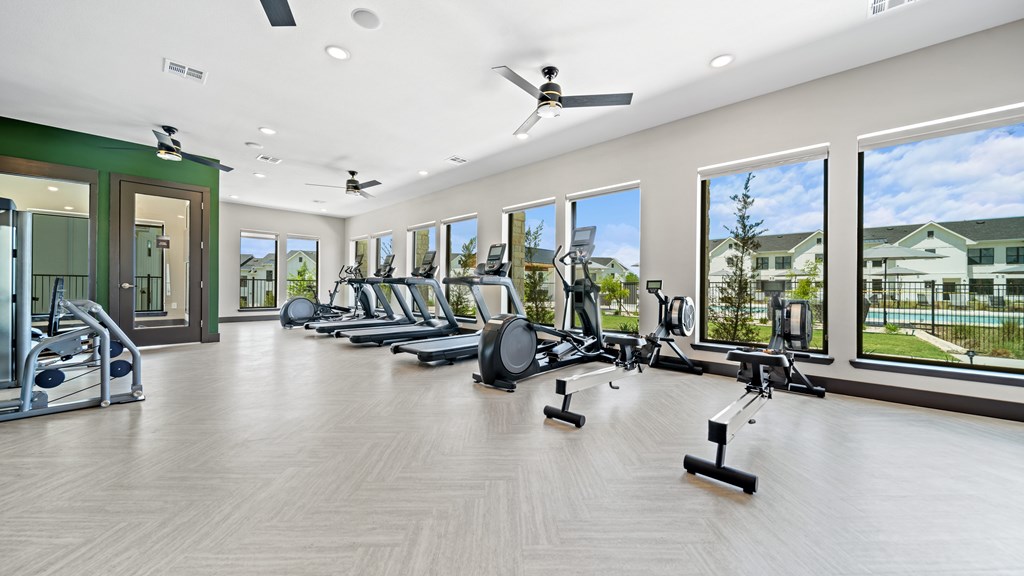 a gym with cardio machines and windows on the wall