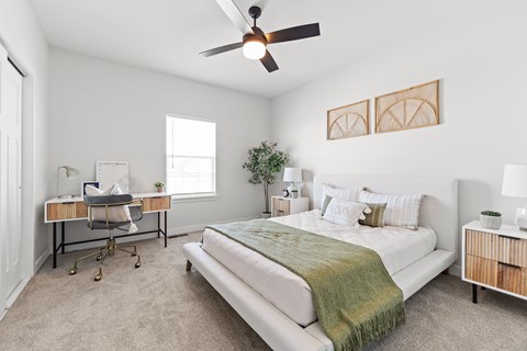 Dog-Friendly townhomes in Raymore, MO - Ascend - Spacious Bedroom With Large Bed, Nightstands With Lamps, Ceiling Fan, Plush Carpet, Work Desk, And Large Window.