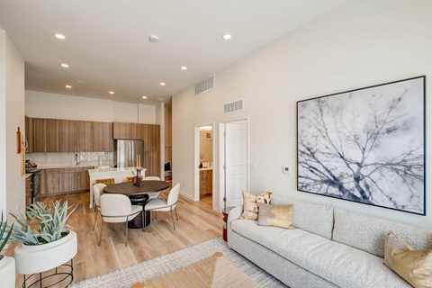 A living room with a grey couch, a table with chairs, a potted plant, and a large painting on the wall.