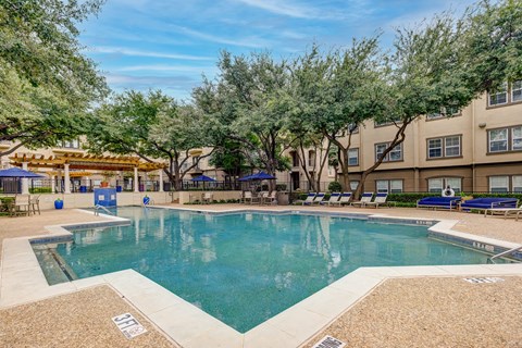 A large swimming pool surrounded by trees and lounge chairs.