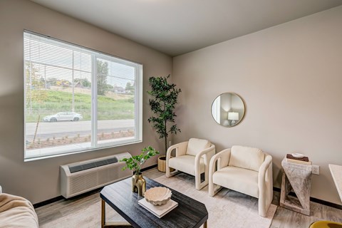 A living room with a large window, a couch, a chair, a coffee table, and a potted plant.
