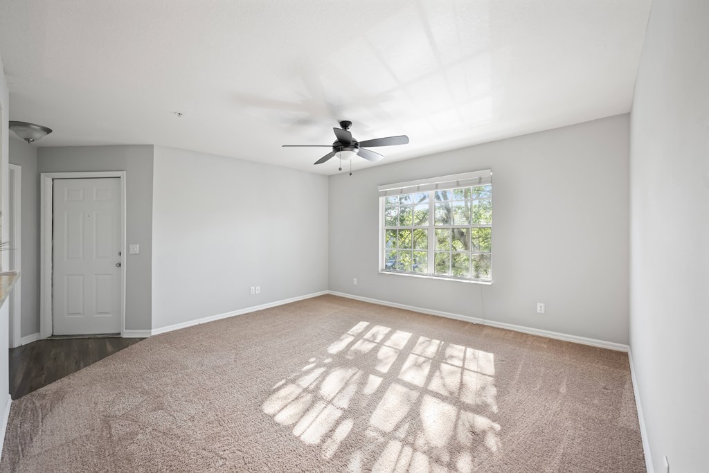 an empty living room with a ceiling fan and a window