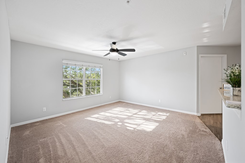 an empty living room with a ceiling fan and a window