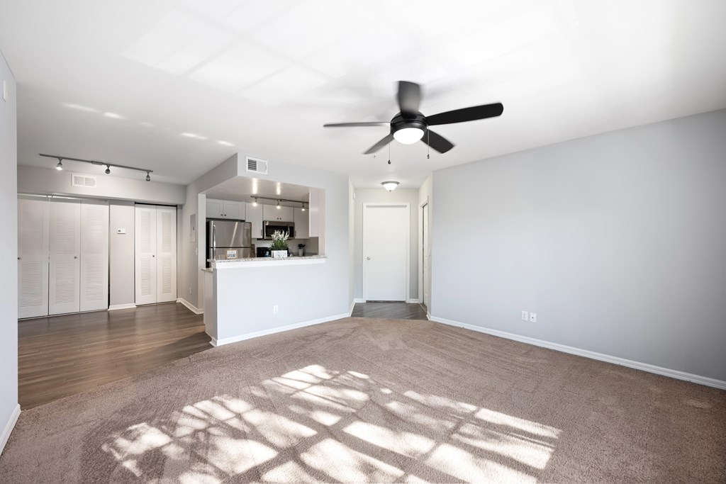 an empty living room with a ceiling fan and a kitchen