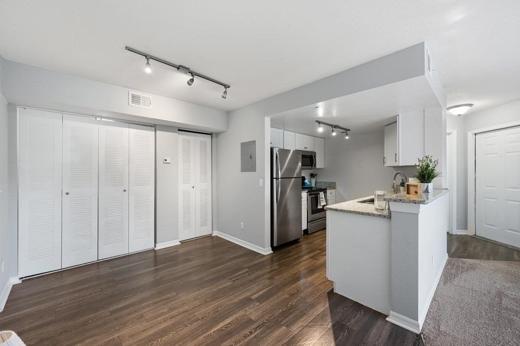an open living room with a kitchen with a refrigerator and a sink