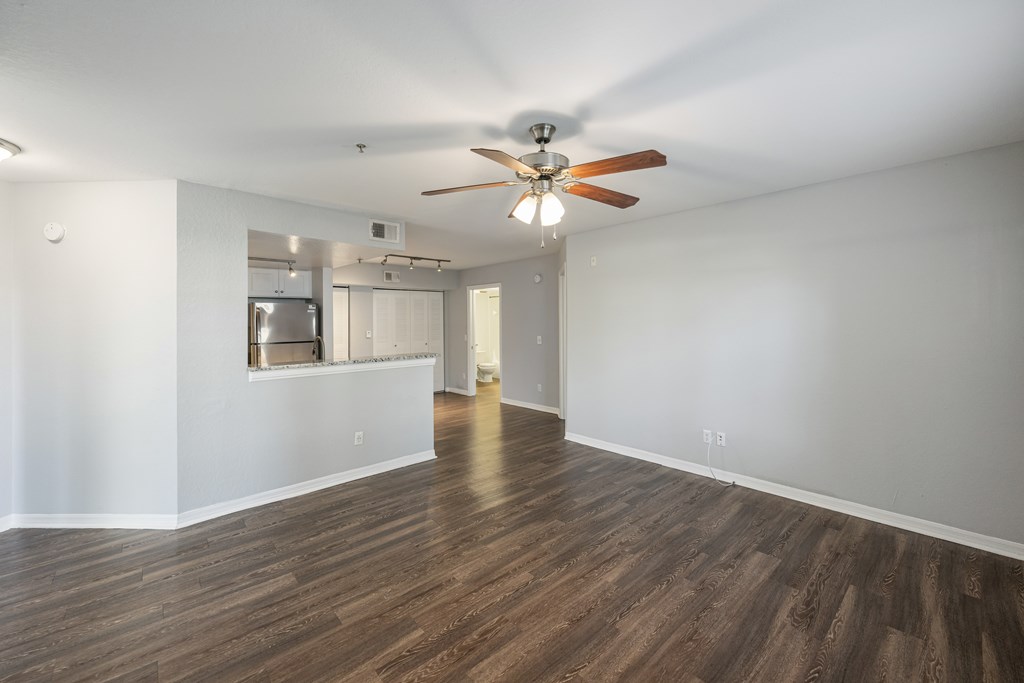 an empty living room with a ceiling fan and a kitchen