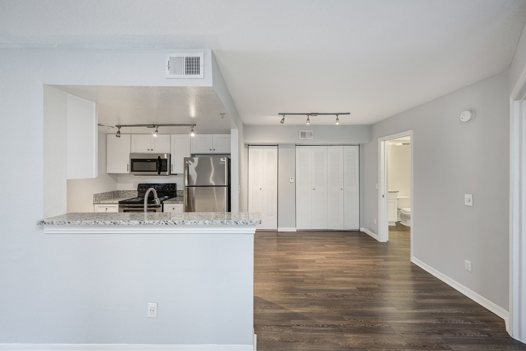 the living room and kitchen of an apartment with white walls and wood flooring