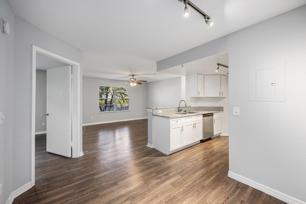 a renovated living room and kitchen with white cabinets and wood floors