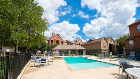 A swimming pool surrounded by a black fence and chairs.