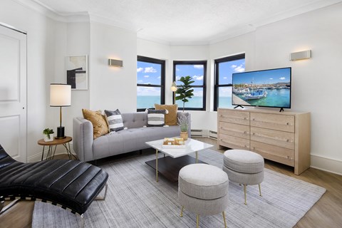 A modern living room with a grey sofa, a black leather chair, a white coffee table, and a television displaying a coastal scene.