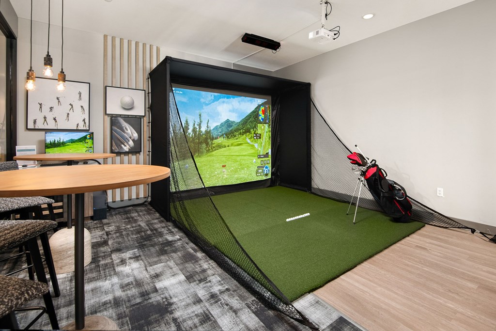 a golf simulator in a room with a table and chairs