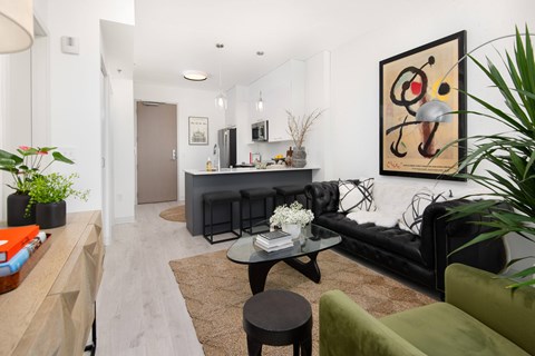 A living room with a black couch, a coffee table, and a painting on the wall.
