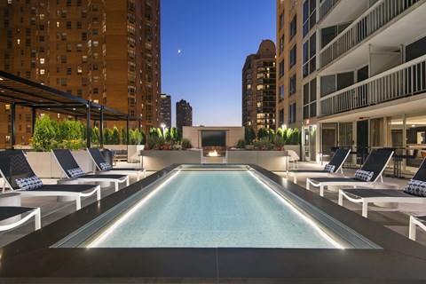 A swimming pool surrounded by lounge chairs in a city setting.