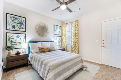 A bedroom with a bed, dresser, mirror, and artwork.