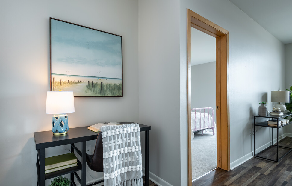 a desk with a lamp and a mirror in a room with a bedroom in the background