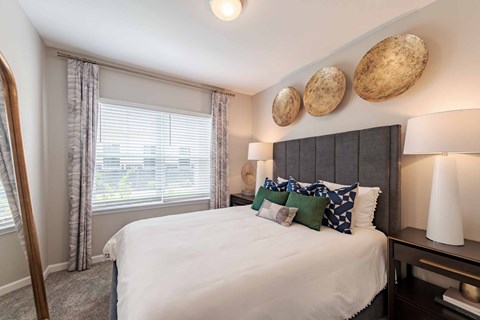 A bedroom with a large bed and a window with blinds.