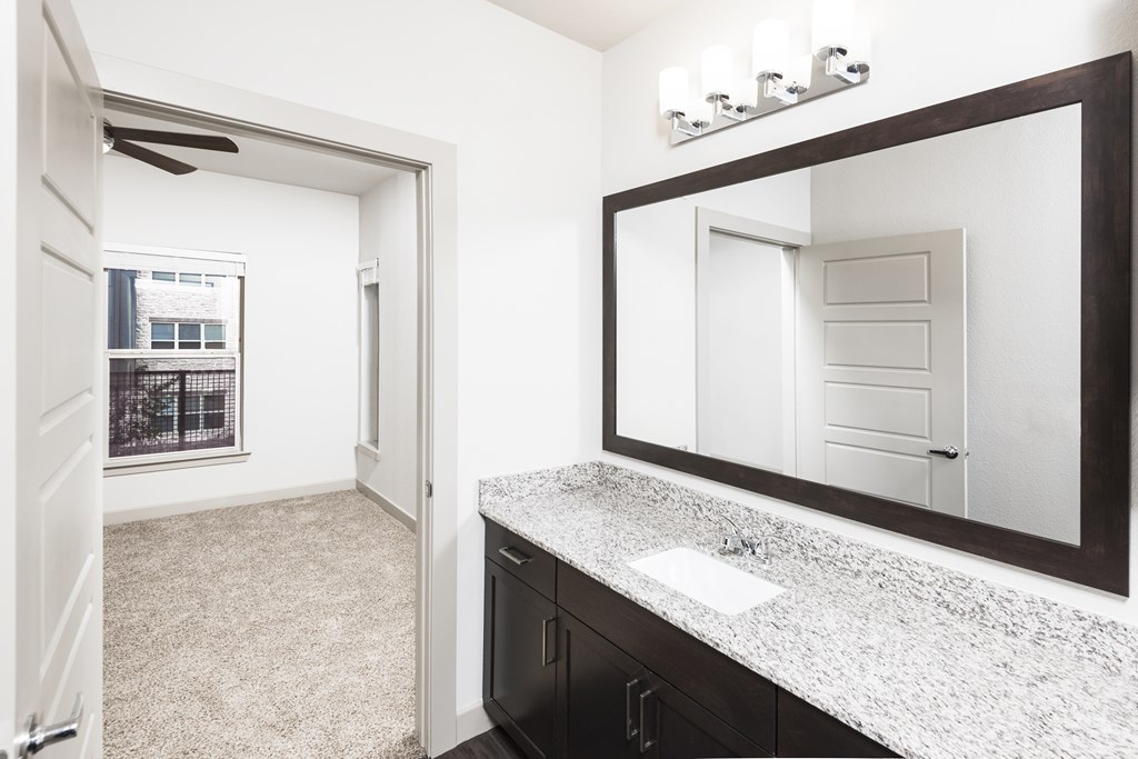 a bathroom with a sink and a mirror and a door to a bedroom