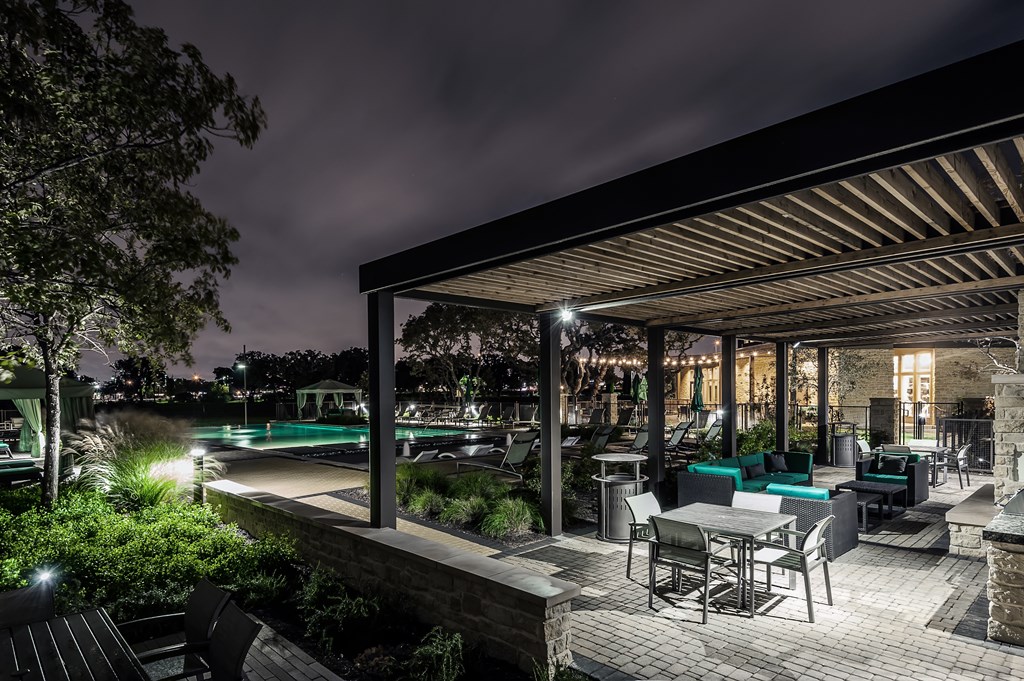 a patio with tables and chairs and a pool at night