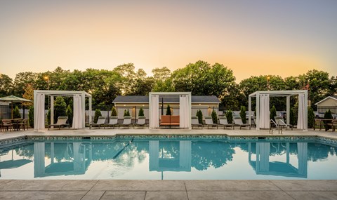 A pool surrounded by lounge chairs and trees.