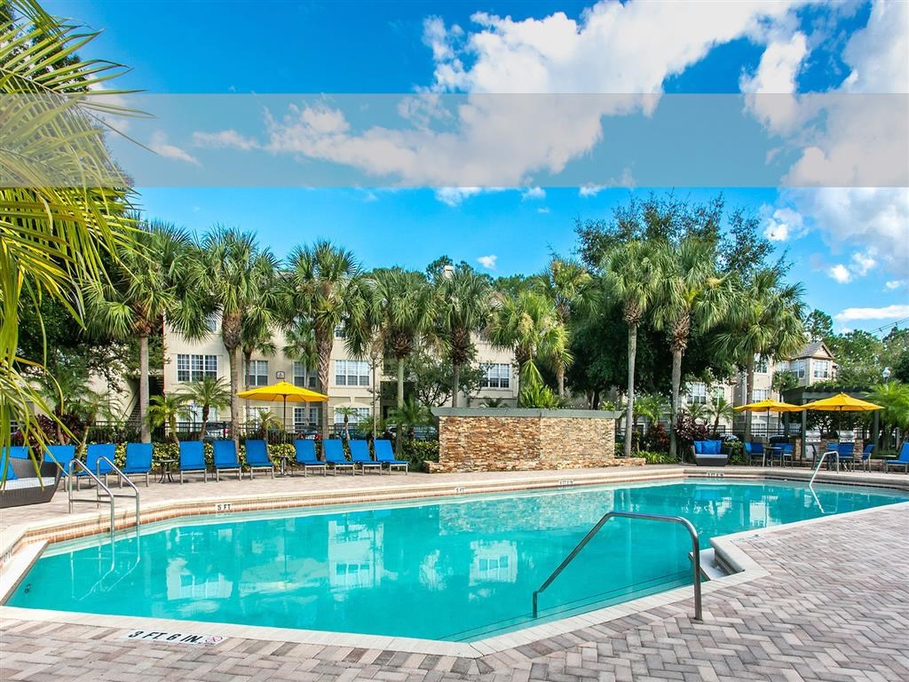 a large swimming pool with blue chairs and palm trees