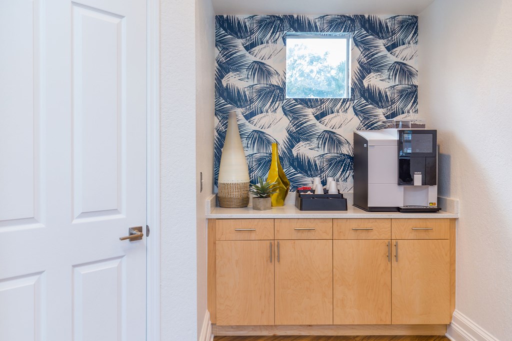 a kitchenette with a coffee machine and a mirror with a palm leaf pattern on the wall