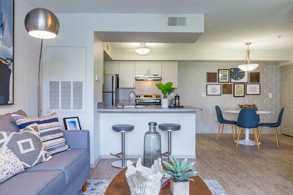 a living room with a couch and a table with stools in front of a kitchen with
