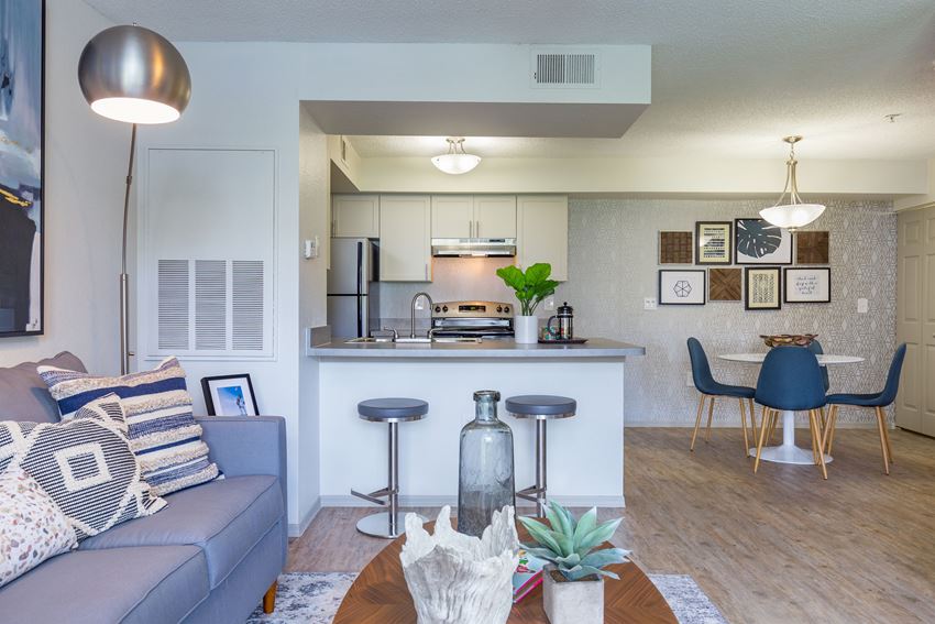 a living room with a couch and a table with stools in front of a kitchen with - Photo Gallery