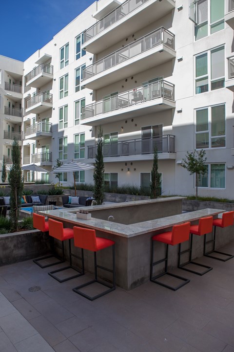 A white building with balconies and a pool table with red chairs in front.