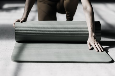 A person is holding a rolled-up grey mat.