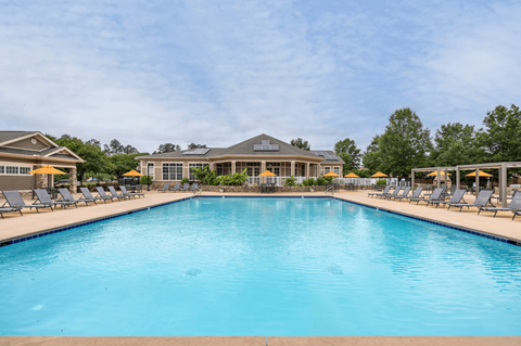 A large swimming pool in front of a building with lounge chairs on either side.