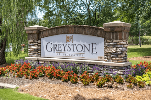 A sign that says "Greystone at Widewaters" is surrounded by flowers.