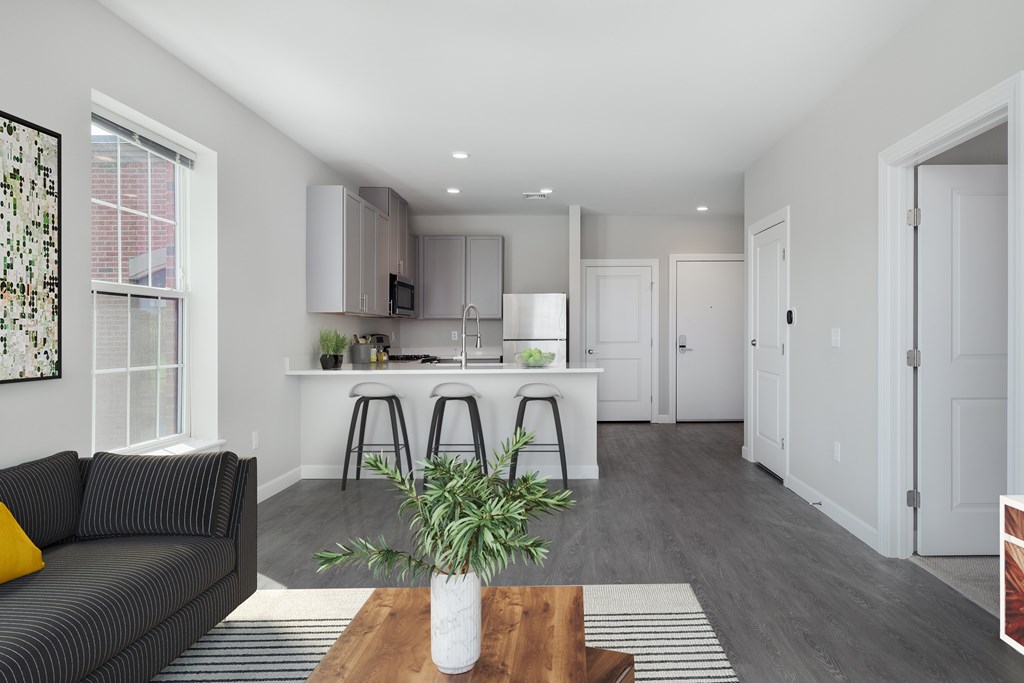 A modern living room with a grey sofa and a kitchen area in the background.