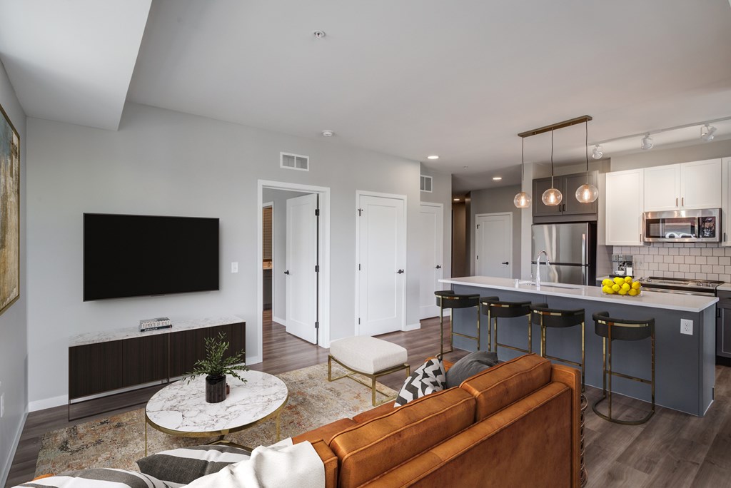 a living room with a couch and a table with three stools in front of a kitchen