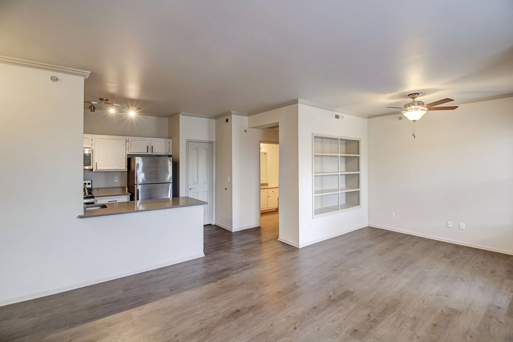 an empty living room with a kitchen in the background
