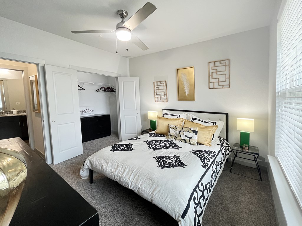 Carpeted bedroom with natural light, ceiling fan, and a spacious closet with french doors.