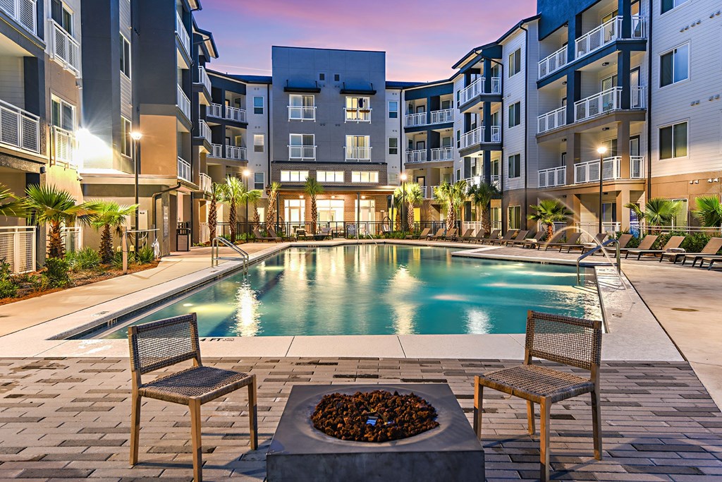 an apartment pool with chairs and a fire pit at dusk