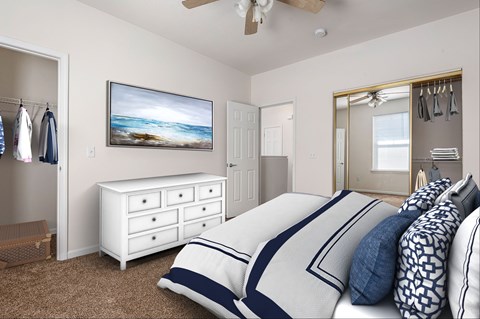 Pet-Friendly Apartments in Lawrence, KS - Ironwood Apartments and Townhomes - Bedroom with Carpet Flooring, Bed, Dresser, Wall Painting, Ceiling Fan, and Oversized Closets with Mirrored Sliding Doors.