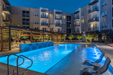 A swimming pool in front of apartment buildings at dusk.