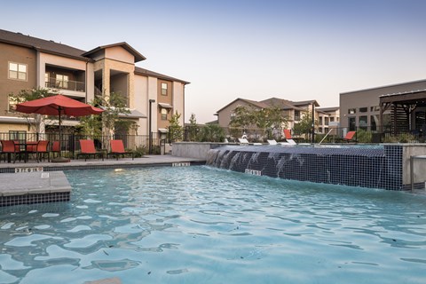 A swimming pool in front of a building with a red umbrella.