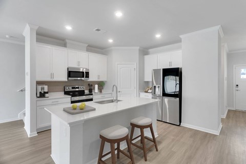 A kitchen with white cabinets and a white island with two stools.