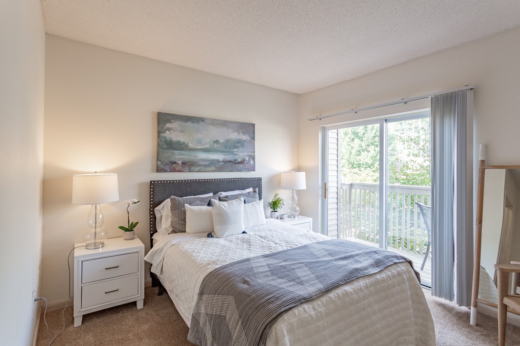 a bedroom with a large bed and a sliding glass door leading to a balcony at Lake Susan Apartments in Chanhassen, MN