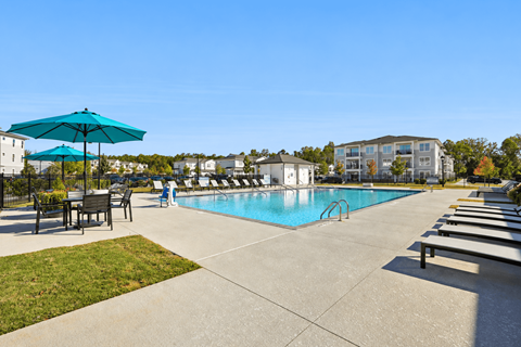 A swimming pool with a blue umbrella and lounge chairs.