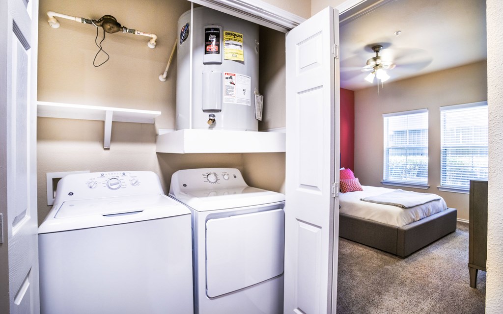 a washer and dryer in a laundry room with a bed in the background
