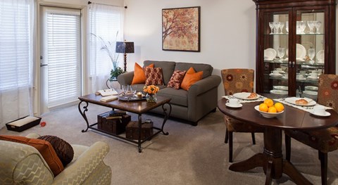 A living room with a grey couch, a coffee table, and a dining table set for two.