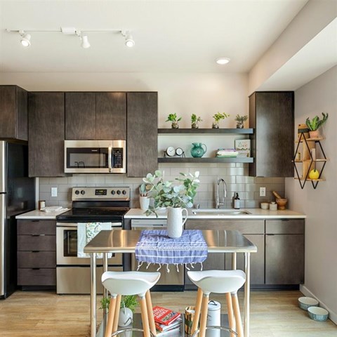 A modern kitchen with a stainless steel oven and microwave, a sink with a faucet, and a dining table with two chairs.