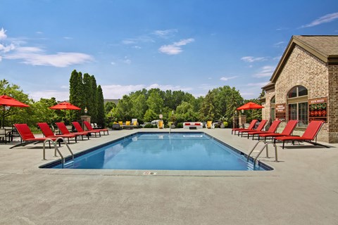A pool surrounded by red chairs and umbrellas.