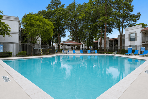 A large swimming pool surrounded by trees and chairs.